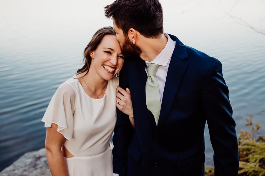 Groom kissing brides forehead in front of lake