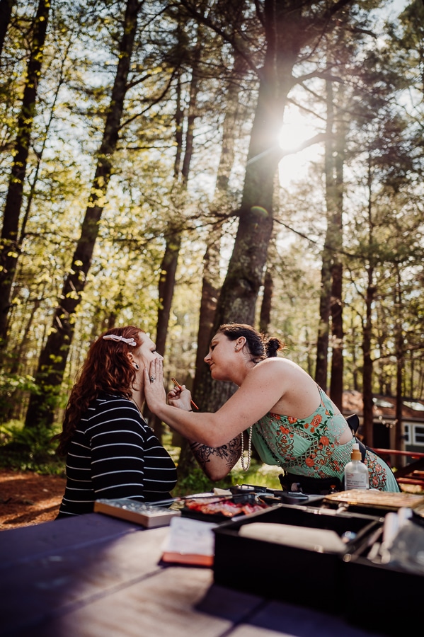 Bride getting makeup done next to woods