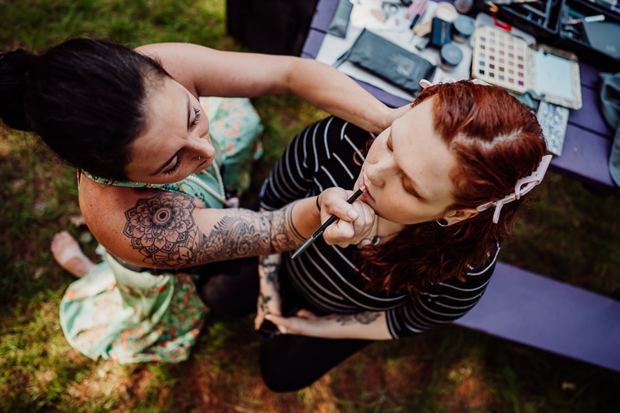 Bride getting makeup done sitting on picnic table