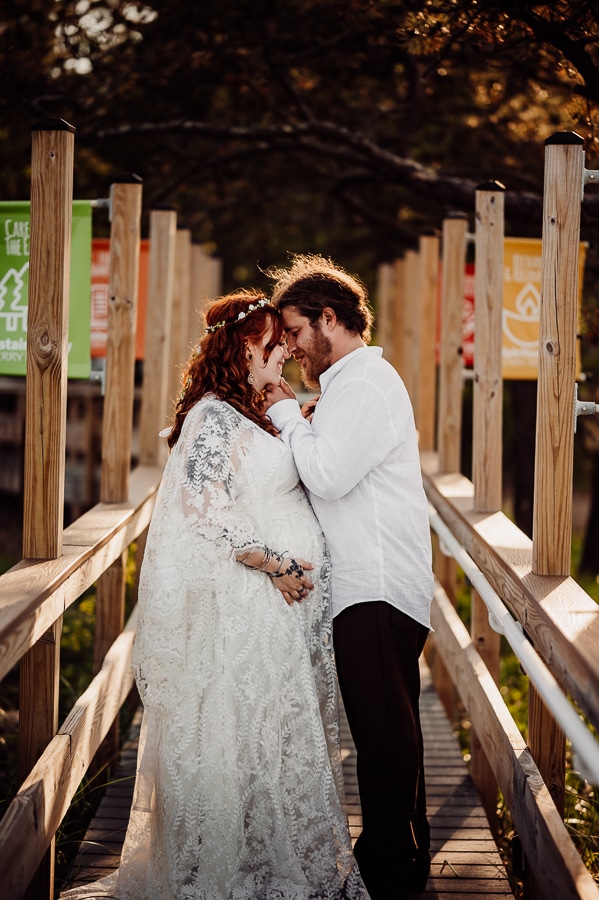 Bride and groom kissing on boardwalk holding belly