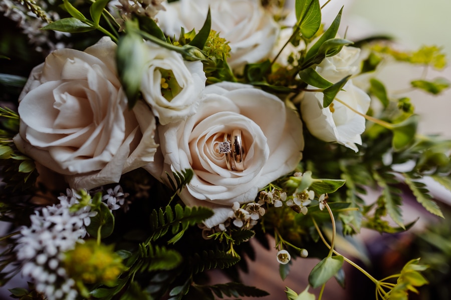 Engagement ring and wedding rings sitting on white rose with green leaves