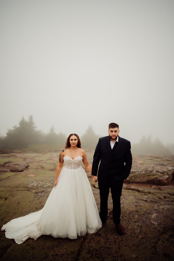 Bride and groom holding hands in fog glaring at camera in acadia