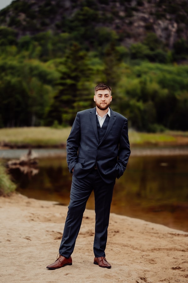 Groom standing with hands in pockets inn front of beehive trail