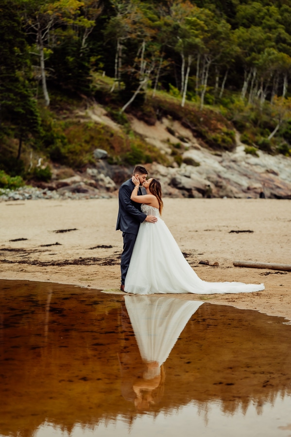 Bride and groom on sand beach in front of reflection of water