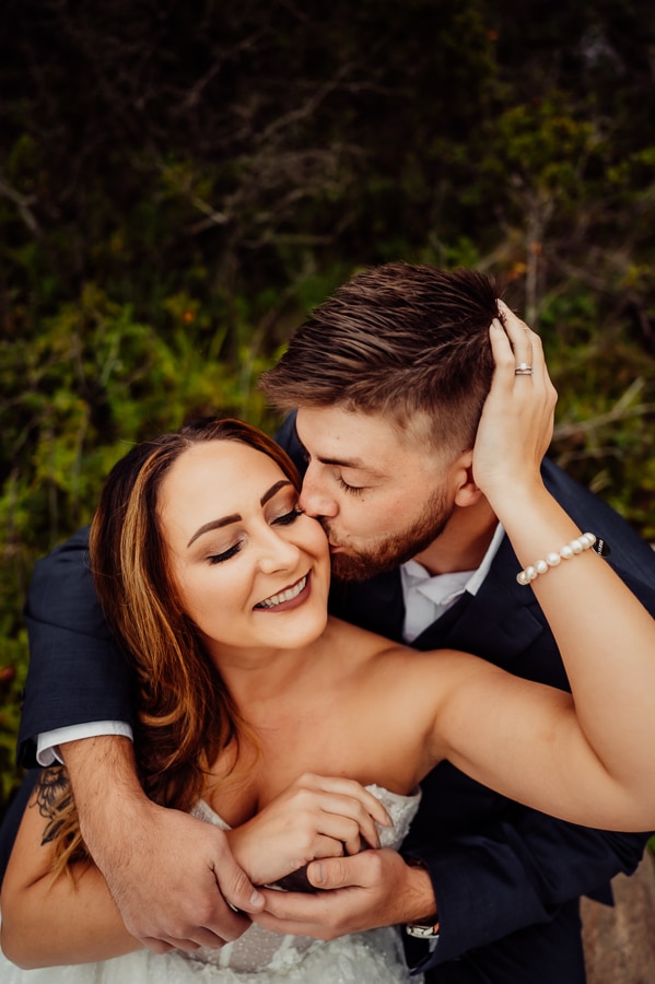 Woman holding husbands head with groom kissing cheek