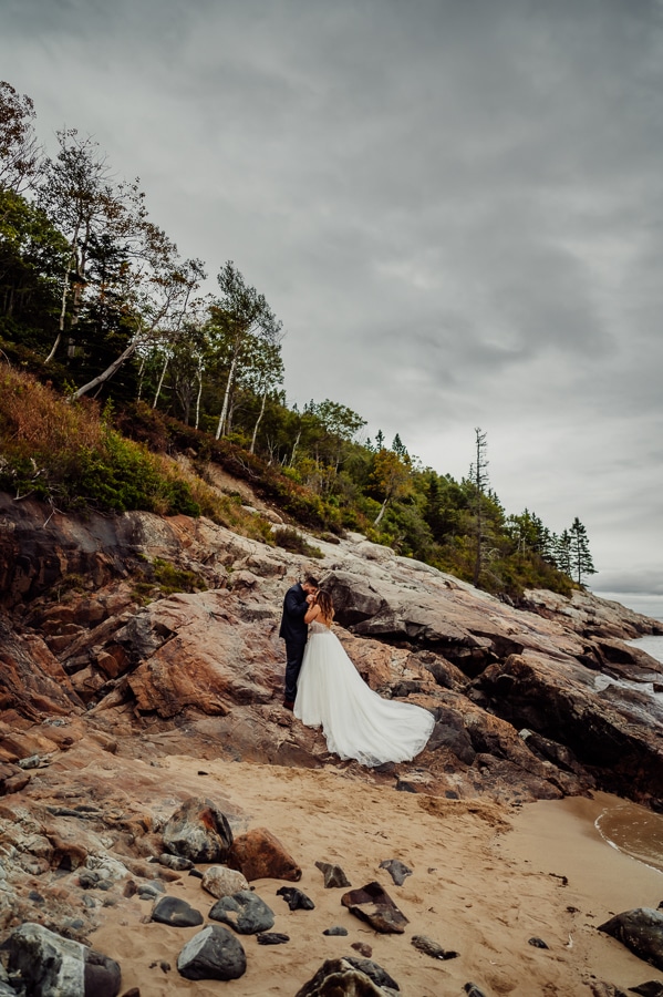 Bride and groom standing on cliff side rocks in Acadia