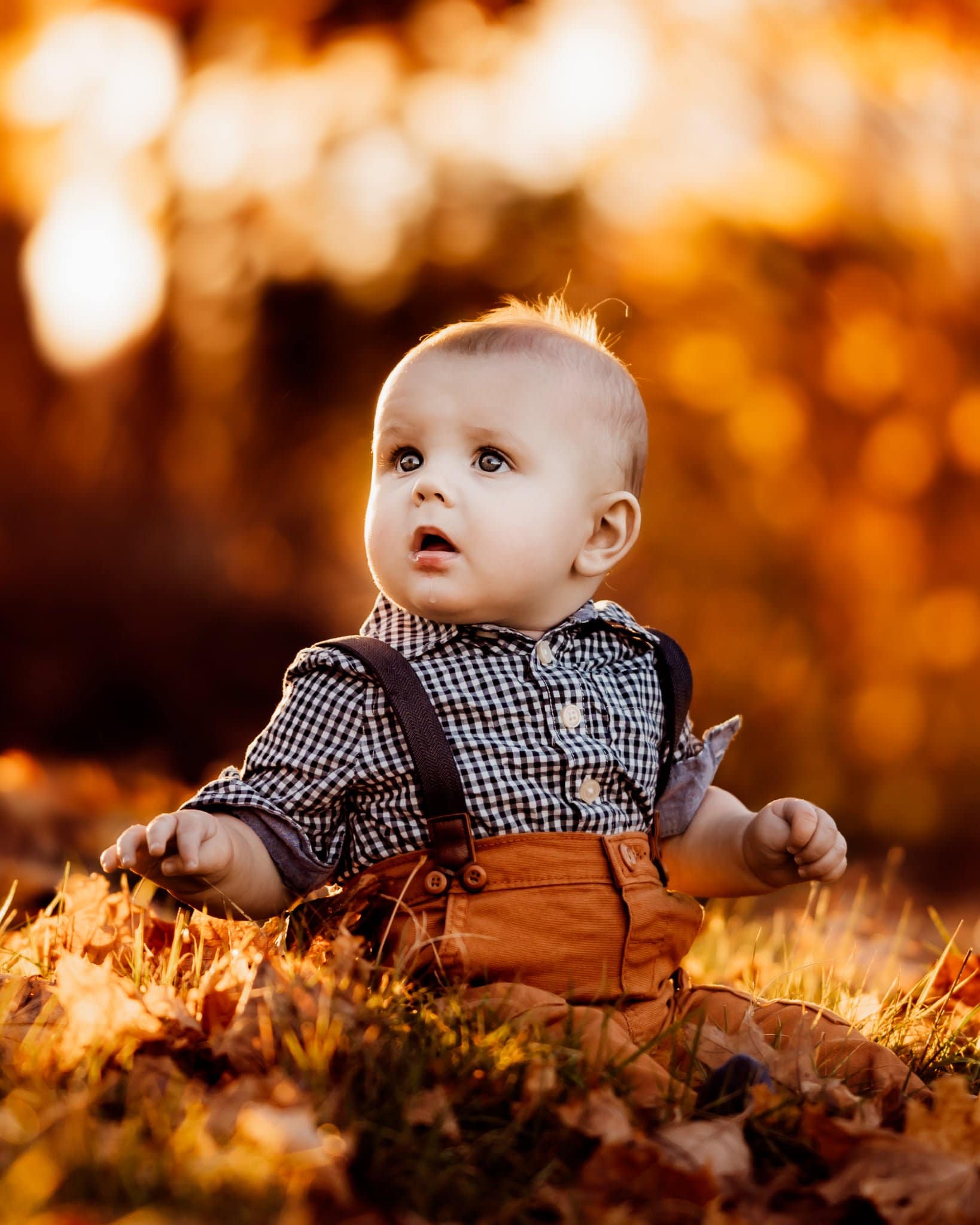 baby boy wearing plaid and suspenders sitting in grass