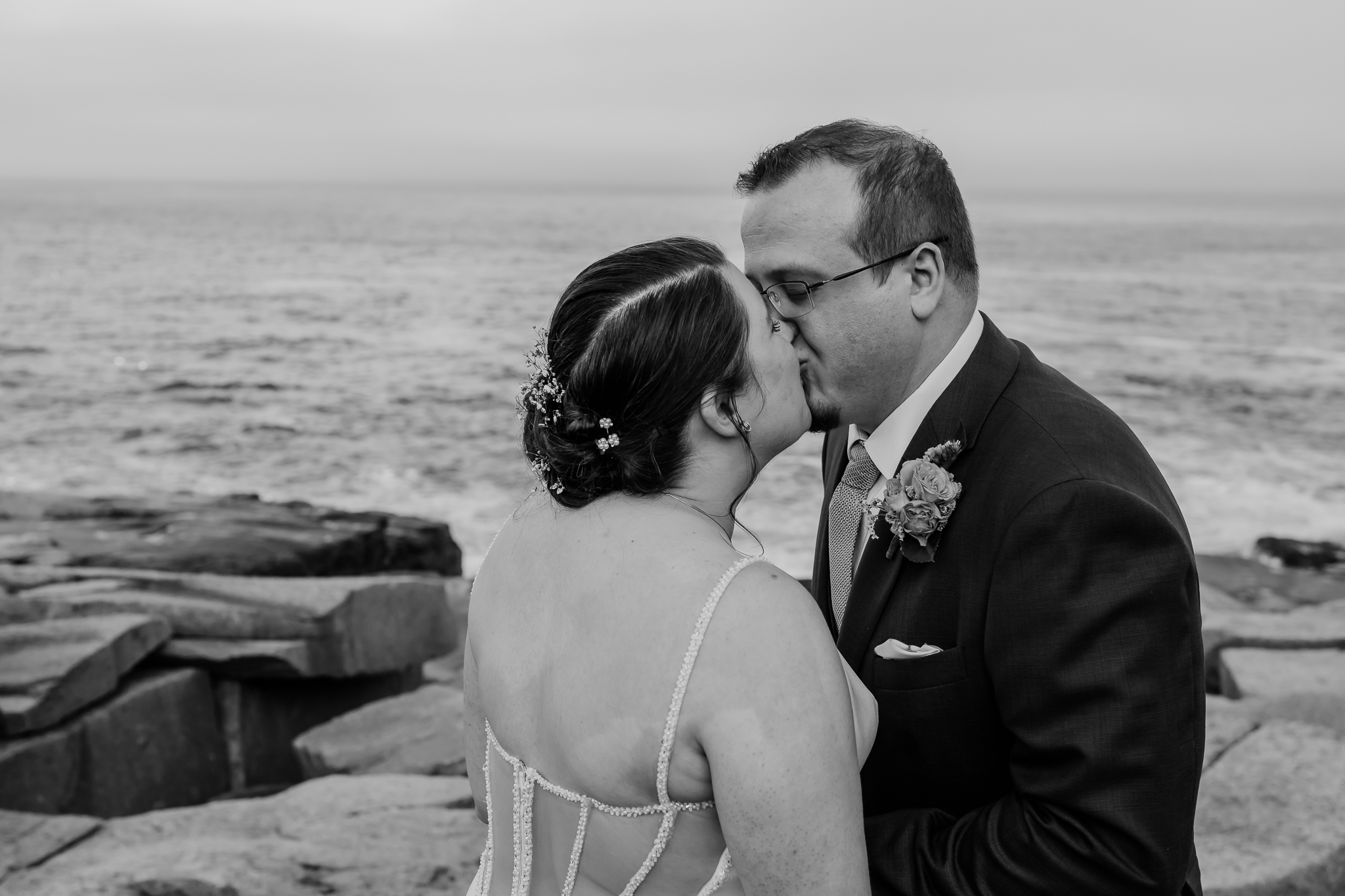 Black and white close-up of bride and groom kissing during their coastal elopement, with the ocean softly blurred in the background.