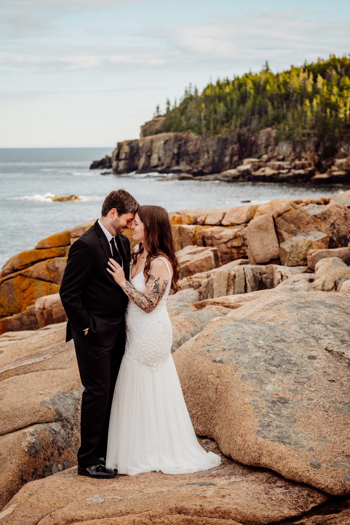 Bride and groom embracing on the granite shoreline of Acadia National Park during a moody coastal elopement session