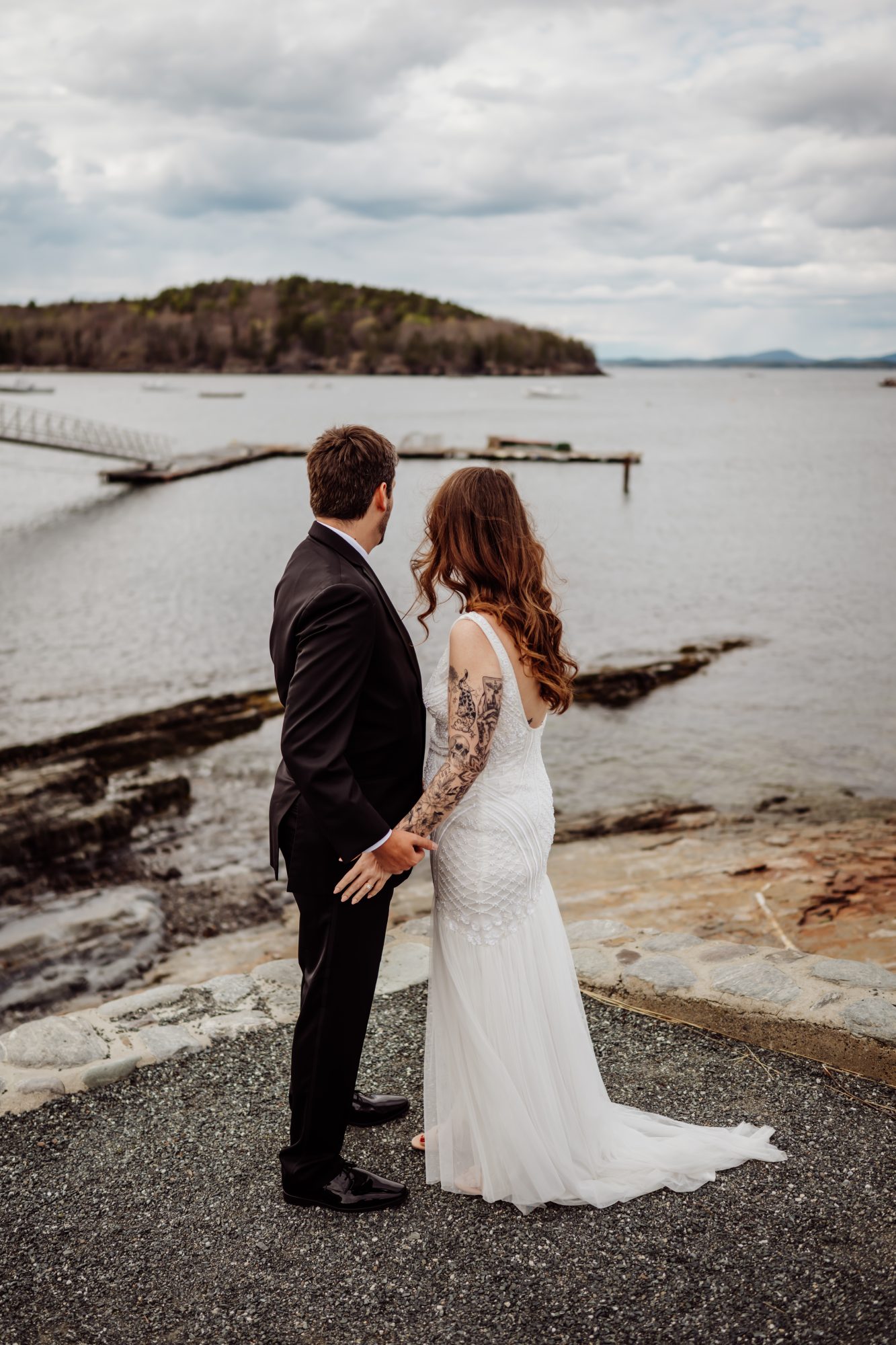 Bride and groom holding hands while overlooking the calm waters of Frenchman Bay on the coast of Maine