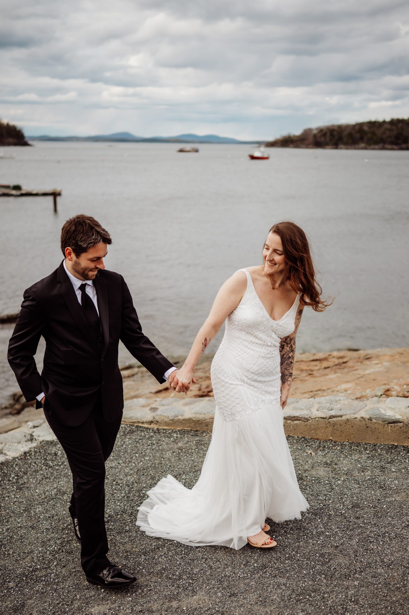 Candid elopement portraits beside the waterfront in Bar Harbor with dramatic clouds over the bay