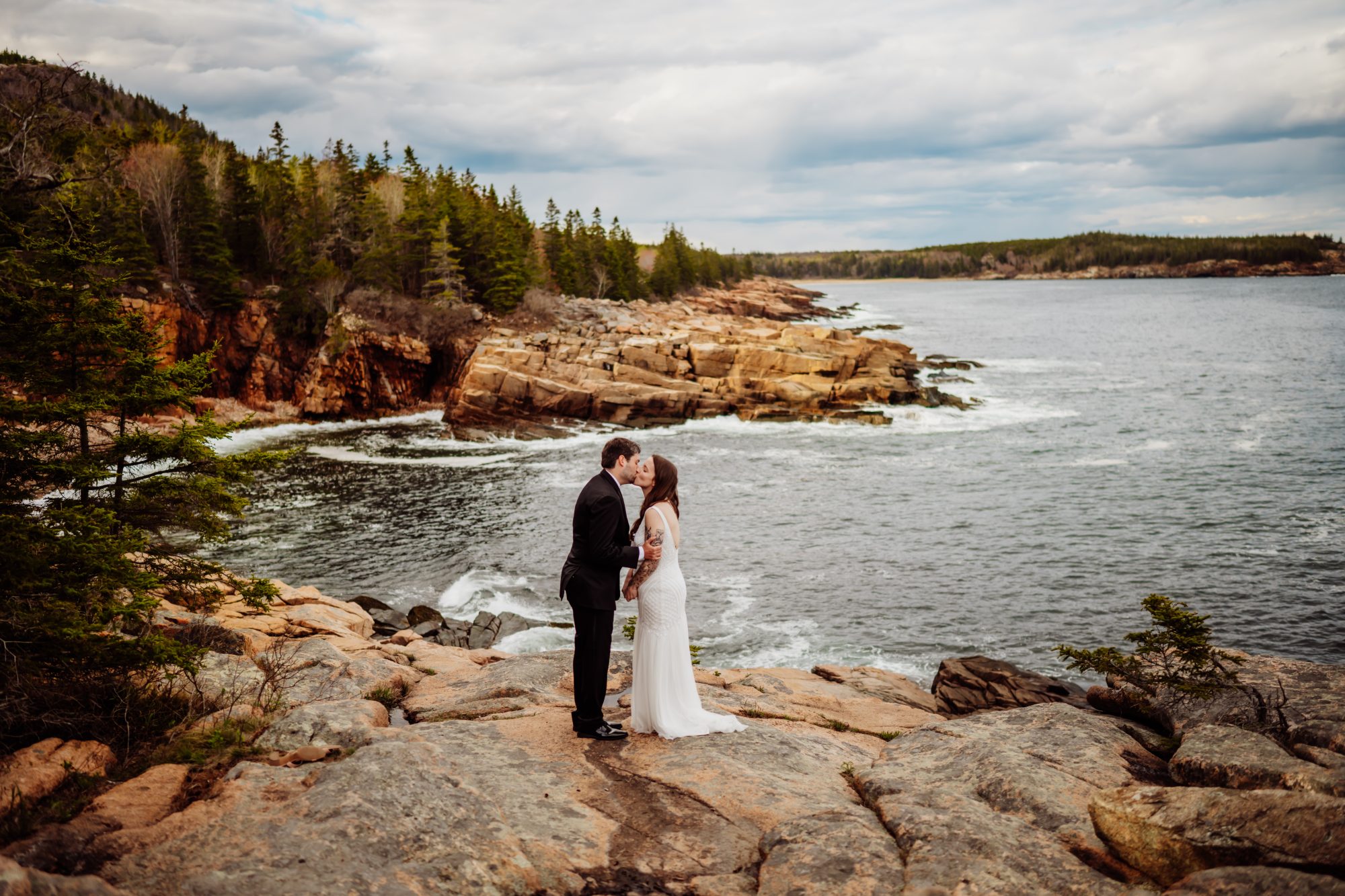 Newly married couple kissing on the cliffs of Acadia National Park overlooking the Atlantic Ocean near Otter Cliffs