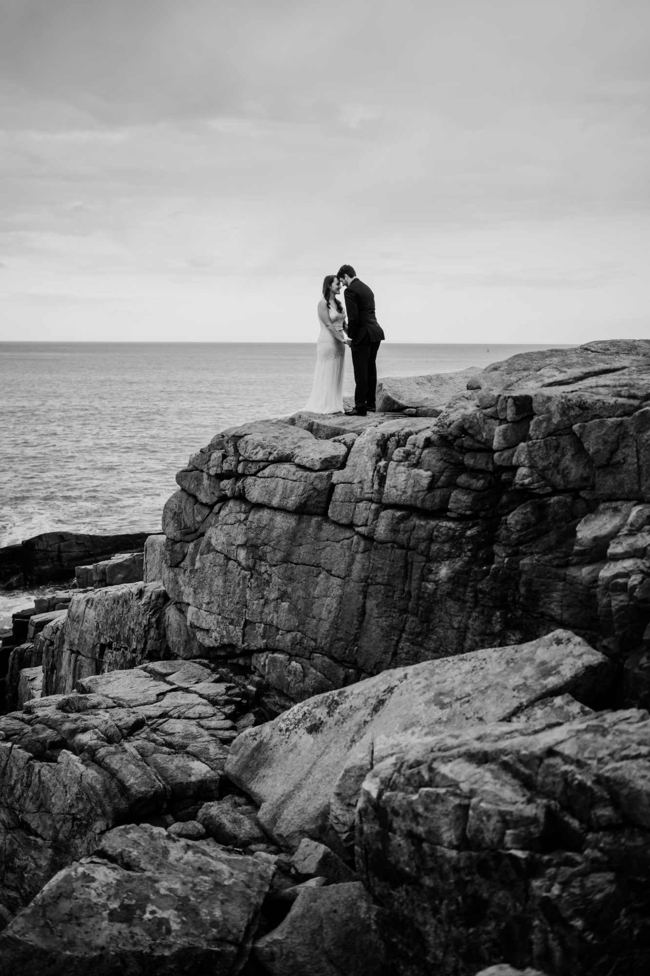 Black and white elopement portrait of a bride and groom standing together on rugged coastal cliffs in Acadia National Park