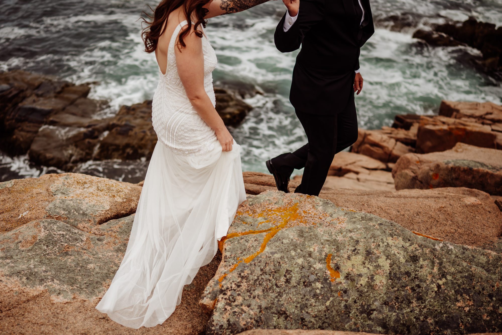 Adventurous couple climbing the rocky shoreline near Otter Cliffs during their Acadia National Park elopement
