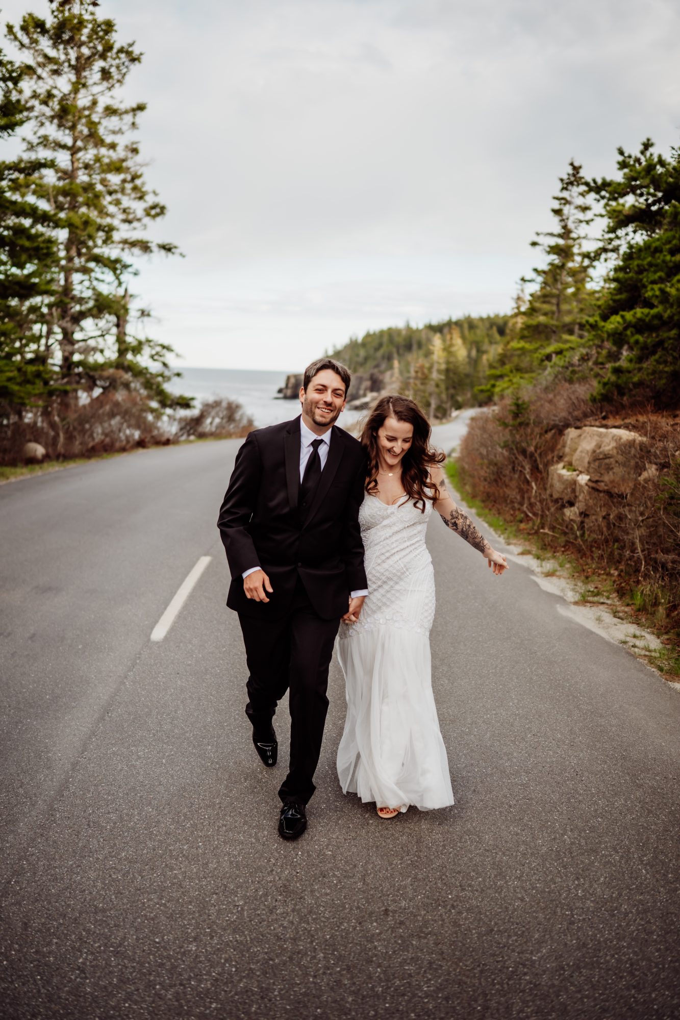 Joyful eloping couple walking down Park Loop Road near Otter Cliffs in Acadia National Park, Maine
