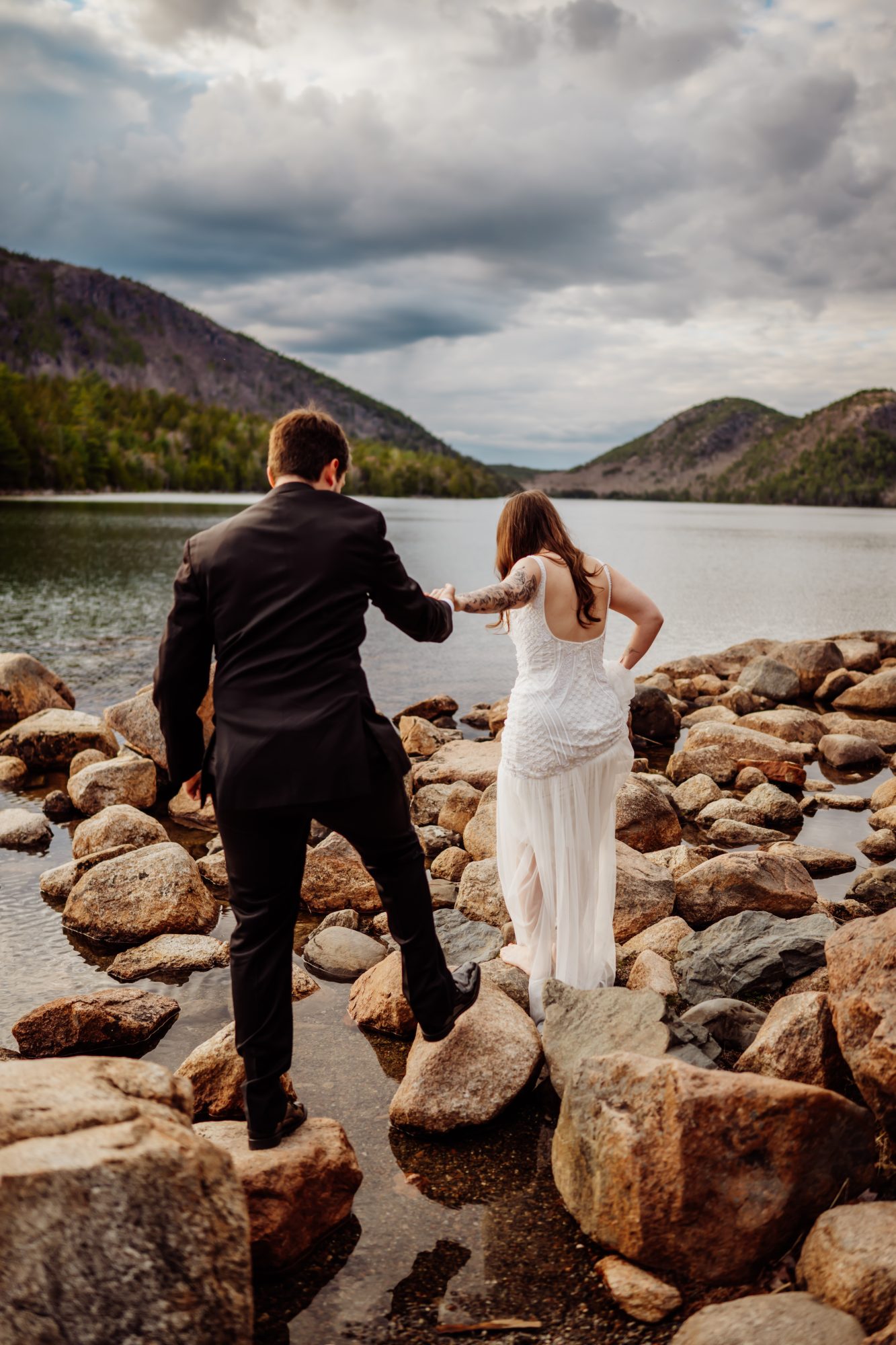 Adventurous couple carefully walking across the rocky shoreline of Jordan Pond in Acadia National Park, Maine