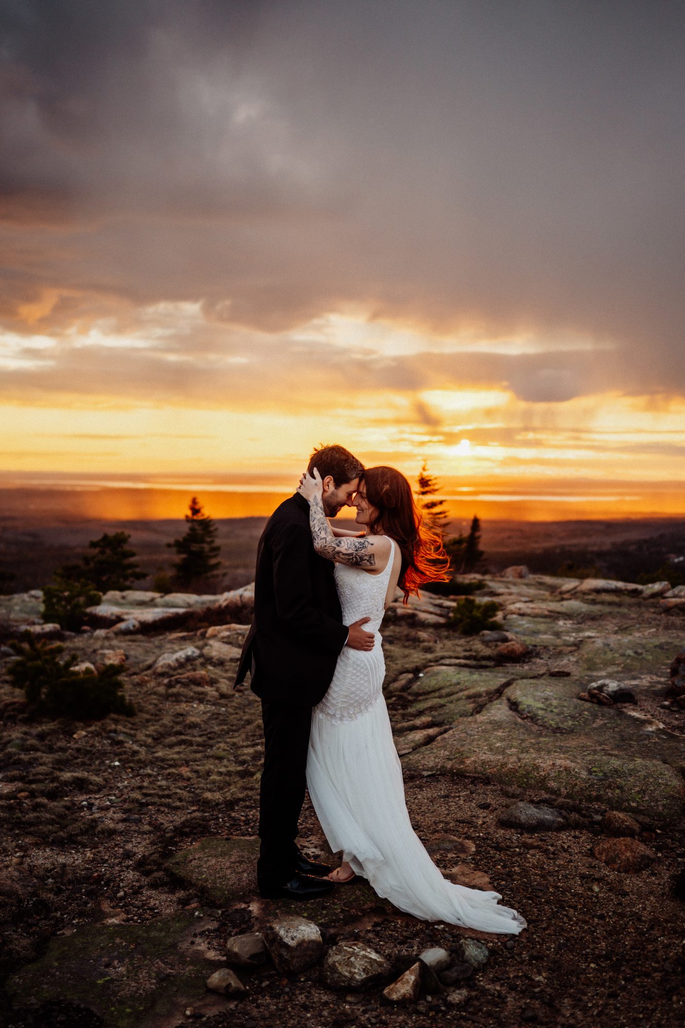 Intimate golden hour elopement photo with bride and groom holding each other on a mountain overlook in Acadia National Park