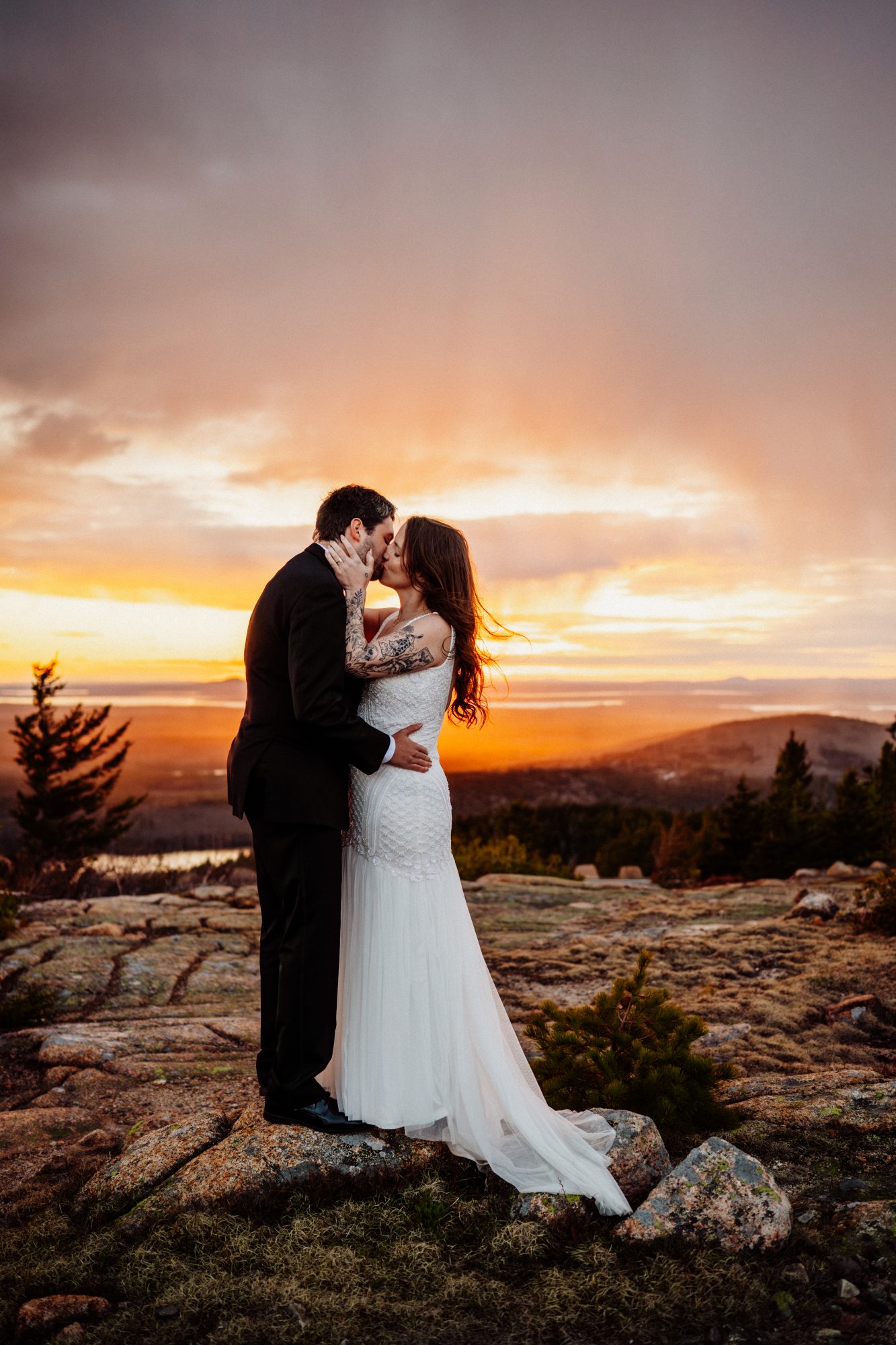 Romantic sunset kiss during an adventurous elopement in Acadia National Park with glowing skies and mountain views