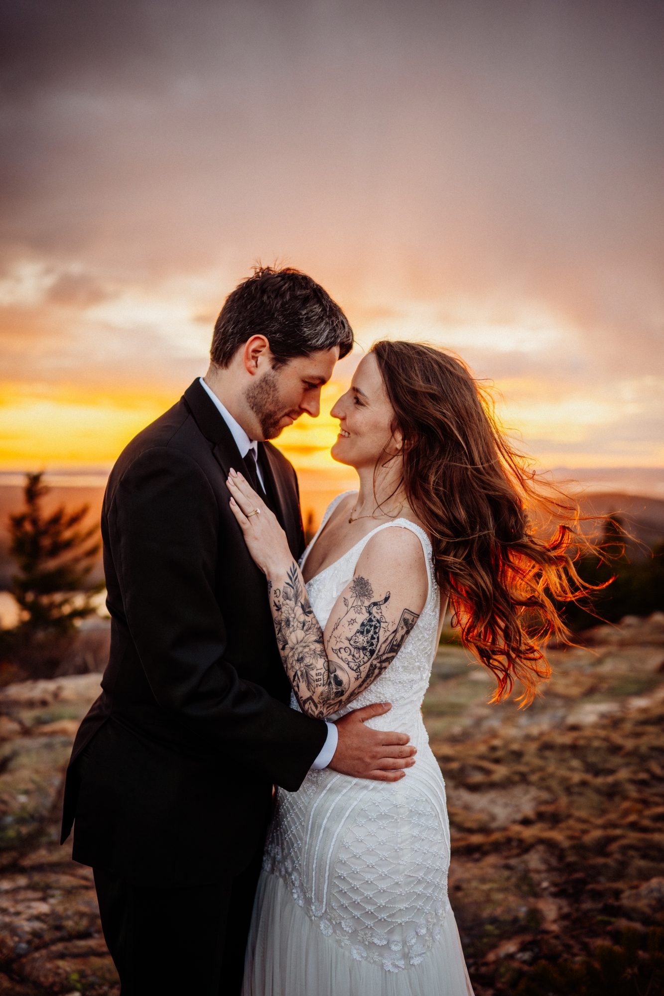 Intimate close-up portrait of an eloping couple embracing at sunset in Acadia National Park with windswept hair and golden light
